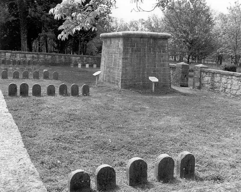 Gravestones and a stone structure in a yard bordered by a stone wall