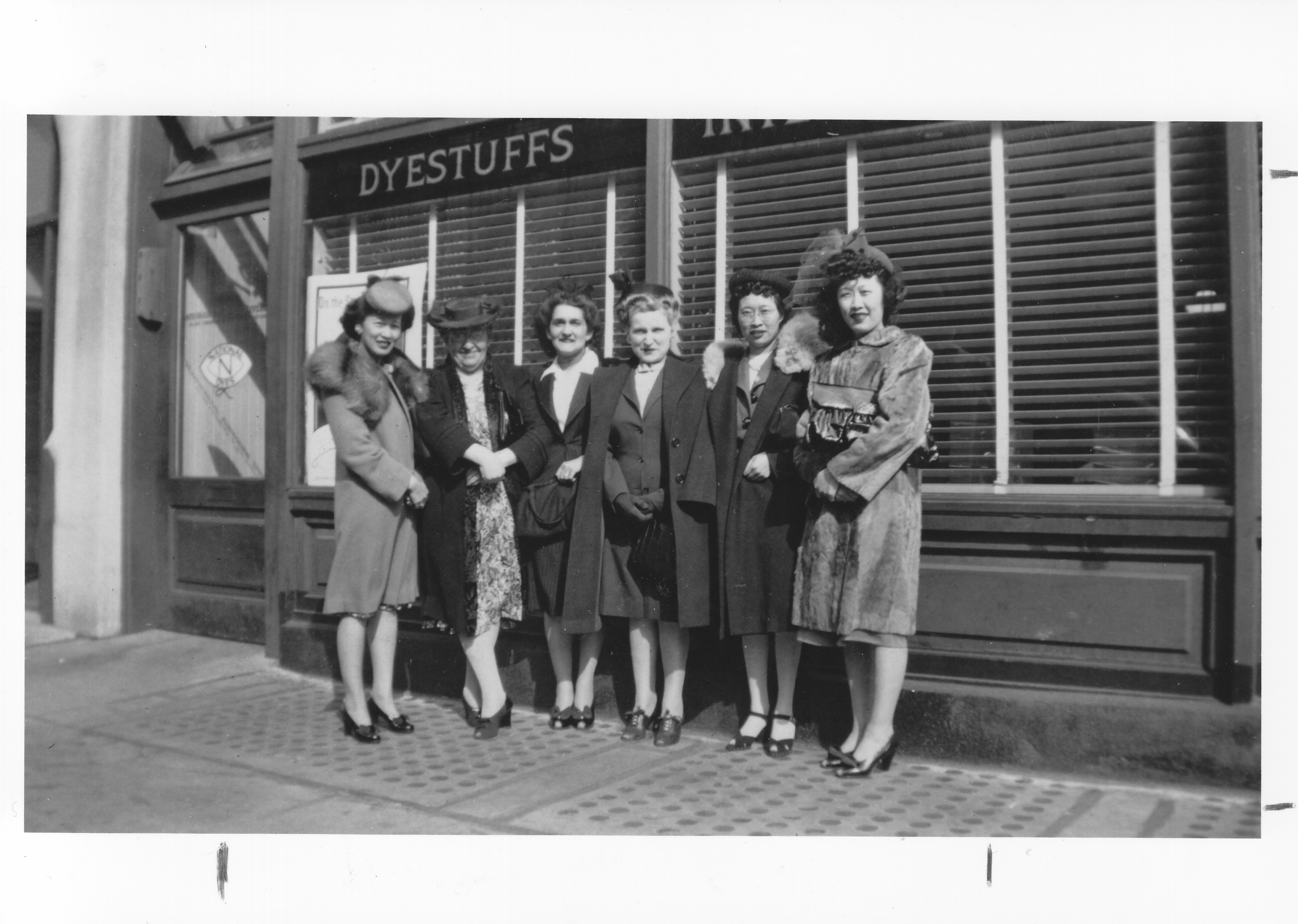 Several women wearing hats, coats, and heels stand outside a storefront.