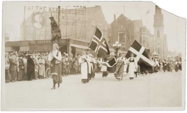 Minnesota Suffrage march 1914 Women in Scandinavian dress holding flags marching down street with crowds on sidewalk