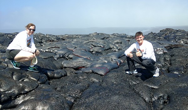 A man and woman check out black lava surface flows at Hawaii Volcanoes National Park.