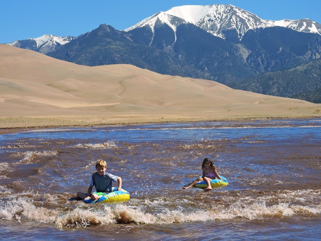 Children use floats to ride the "waves" of Medano Creek at Great Sand Dunes National Park.