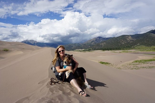 Image of Susan McPartland and her dog Smokey at Great Sand Dunes National Park Susan sitting on a sand dune with her dog Smokey at Great Sand Dunes National Park
