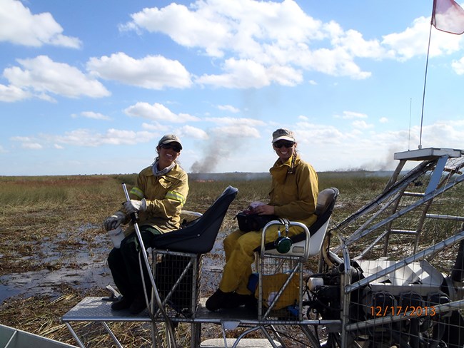 Cynthia Worthington - Florida Fish and Wildlife Two women sit in a vehicle in a wetland with a fire in the background.