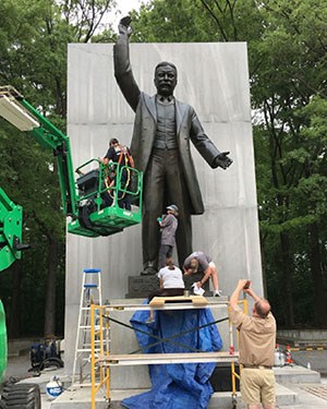 Cultural resource staff on foot and in a bucket lift clean the Theodore Roosevelt memorial statue.