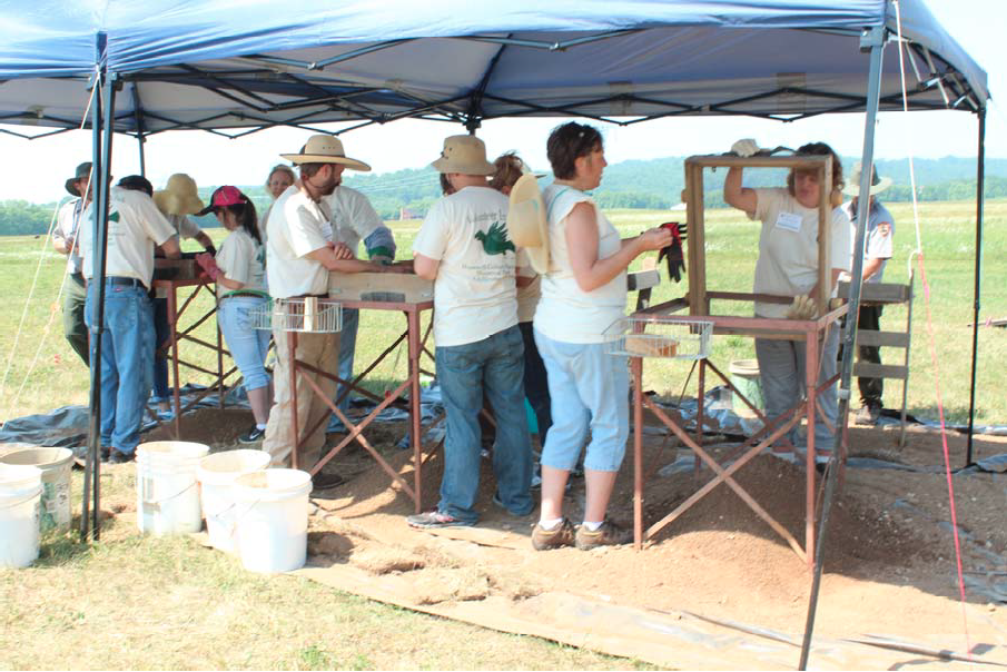 Teachers at work during workshop Several people standing under a tent using tools to sift dirt