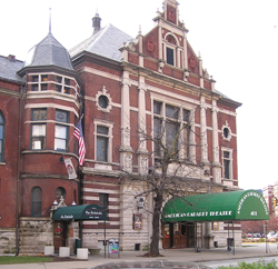 Large brown brick building with large windows and a green awning by the door.