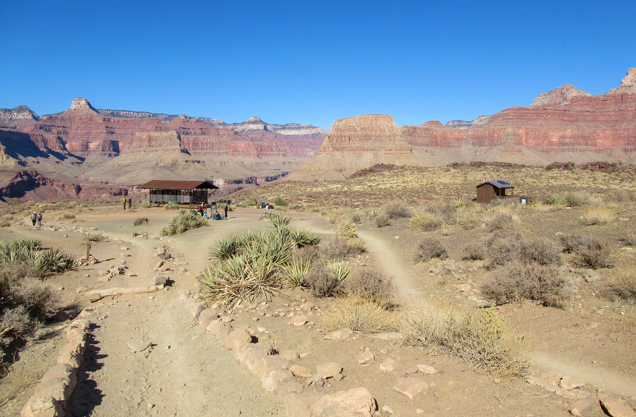 unpaved trails leading to two small buildings in a desert with colorful cliffs in the distance