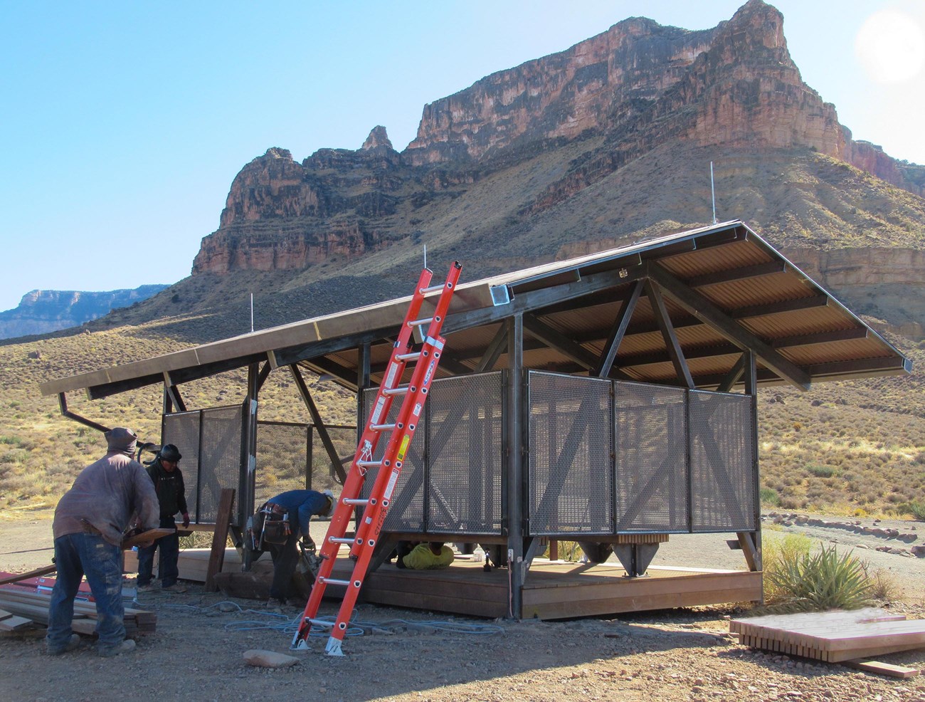 workers completing a 12 x 24 foot shade structure, in a desert, with a canyon wall rising in the distance