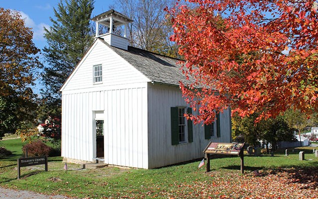 A small, white, wooden chapel amongst autumn-tinged trees.
