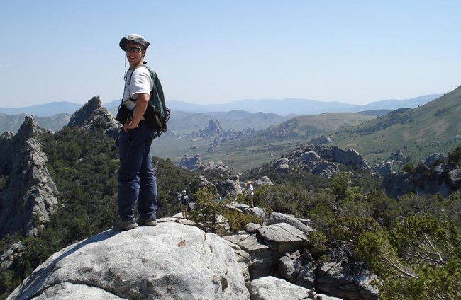 Biologist poses on a large boulder in front of a scenic overlook.