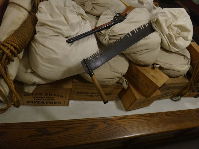 Full burlap sacks with rifle, saw, rope and wooden boxes.
