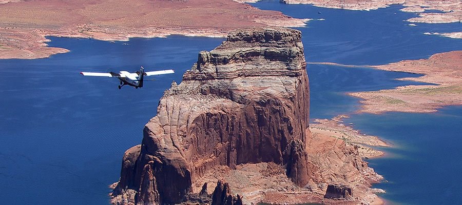 A fixed wing aircraft soars above dramatic rock formations and water at Glen Canyon National Recreation Area. Aerial view above a fixed wing aircraft flying over Glen Canyon National Recreation Area.