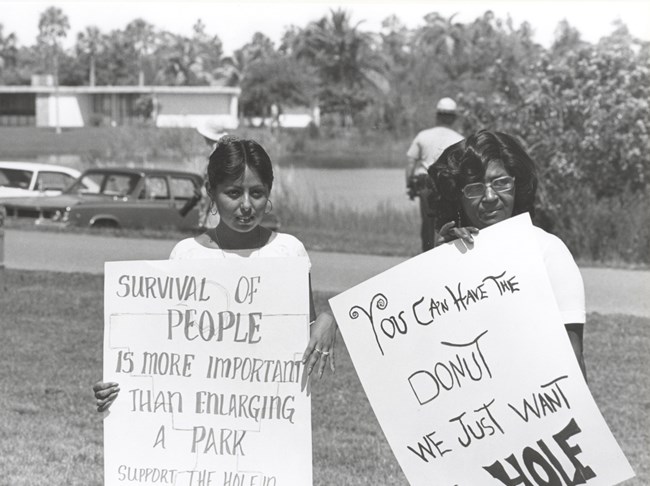 Two protestors with signs with a park ranger behind them Two protestors with signs with a park ranger behind them NPS