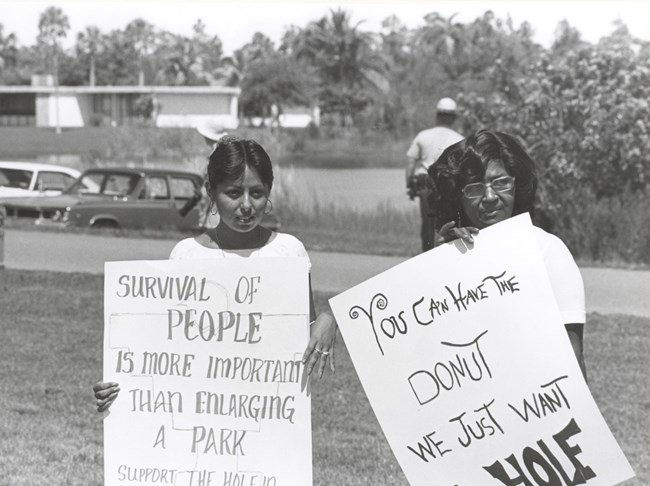 Two protestors with signs with a park ranger behind them NPS