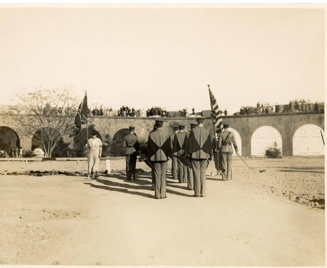 One women holding a Confederate Battle, another women holding an American Flag. Soldiers stand between them inside Fort Pulaski.