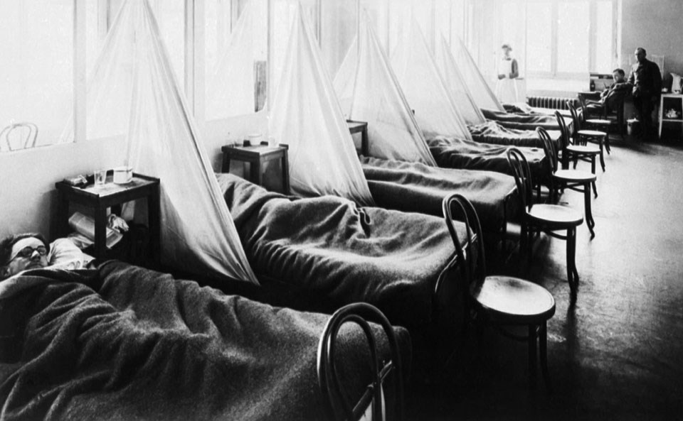 Six beds filled with men stricken with the flu and single chairs at the end of their beds