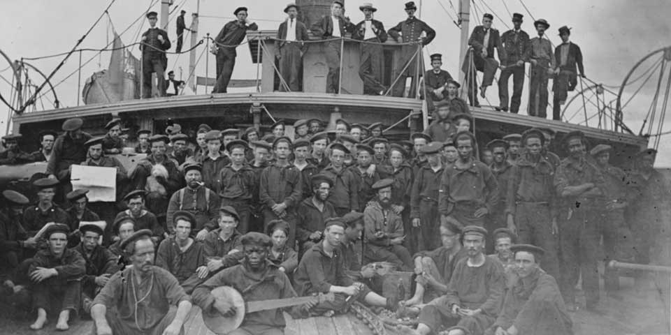 USS Hunchback Crew Black and white photograph of the crew aboard USS Hunchback. Some officers stand on a poop deck while most stand or sit on the main deck.