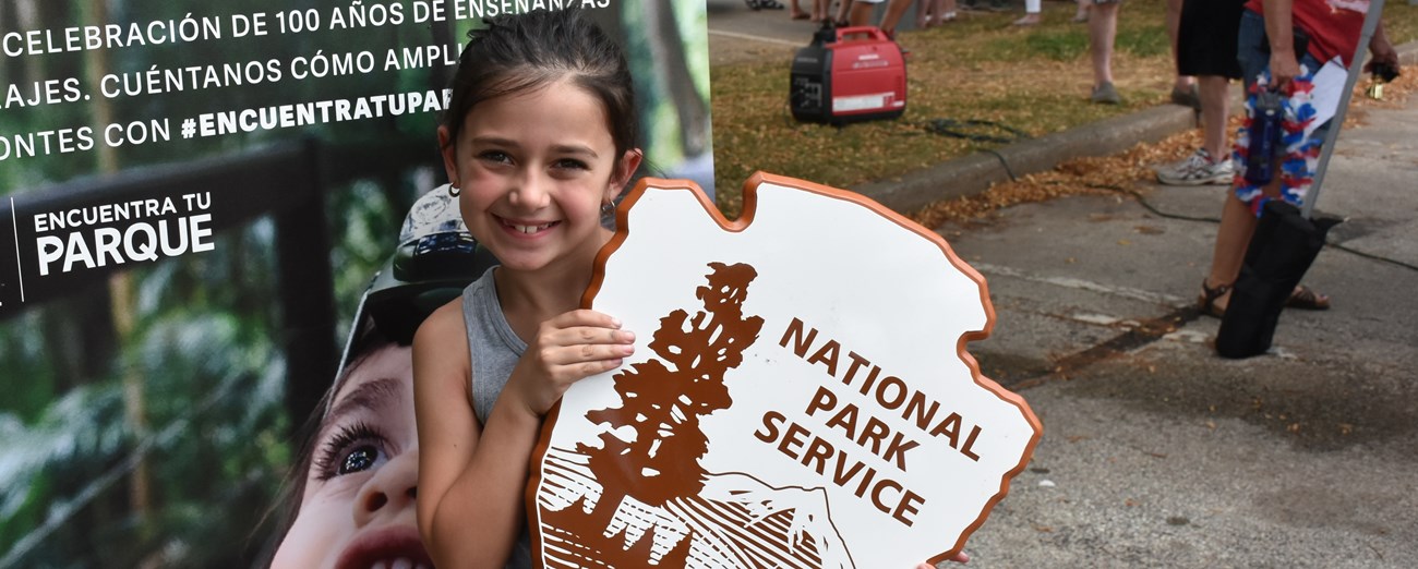 VAFO Find Your Park Child holding up a wooden NPS arrowhead logo