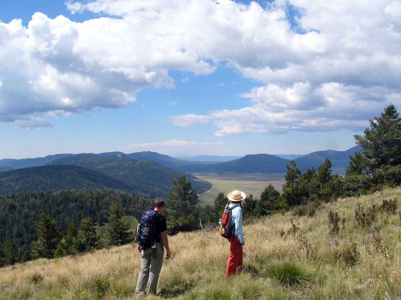hikers on hill slope with valley and hills in background