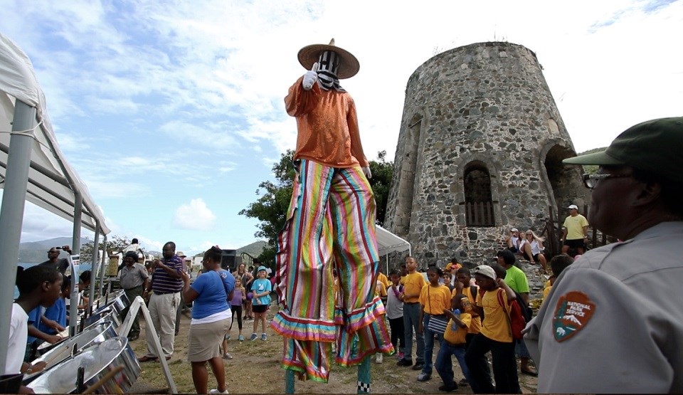 Carnival performer on stilts walking through a crowd near a stone tower