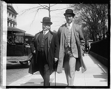 Charles W. and Benjamin W. Morse stroll down the street in three-piece suits and bowler hats.