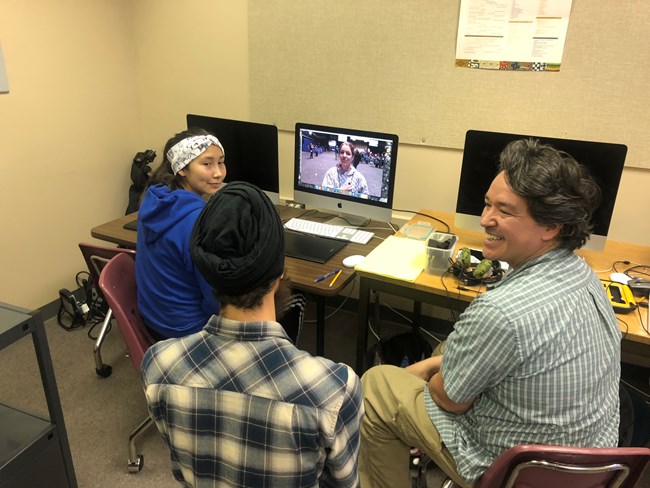 Three people sit around a computer.