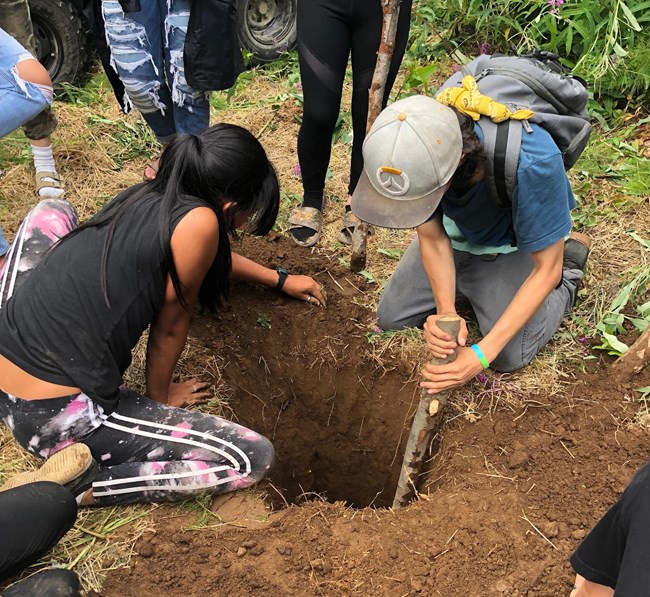 Two kids place a stick down a deep hole while others watch.