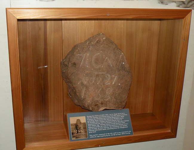 A 1891 stone tablet, once used to mark the location of Washita Battlefield. A large stone inside a glass case on a wall.