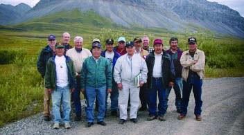 WACH Members A group of 14 men stand on a gravel road in front of a mountain.