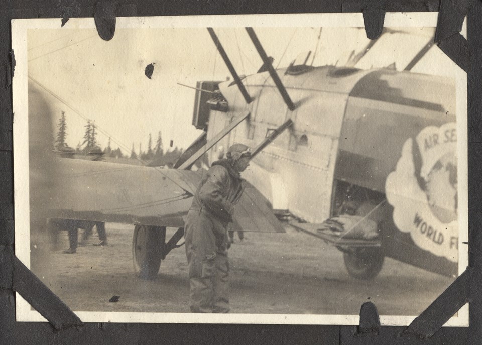 Photo of man in flight suit standing next to a biplane aircraft
