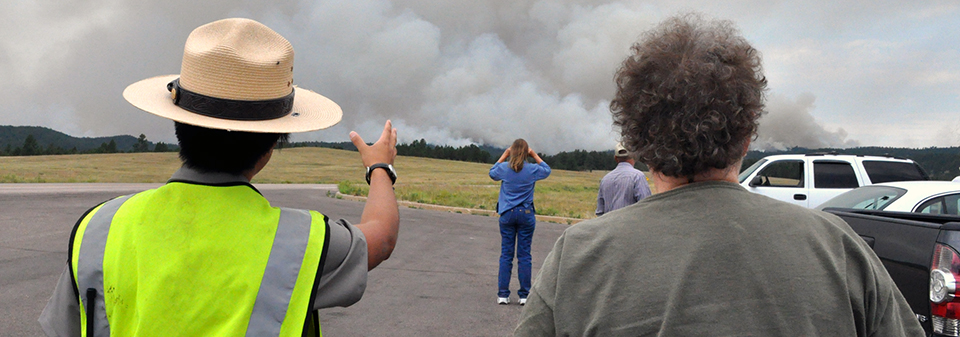 A ranger points to a smoke plume while standing next to a man. A ranger points to a smoke plume while standing next to a man.