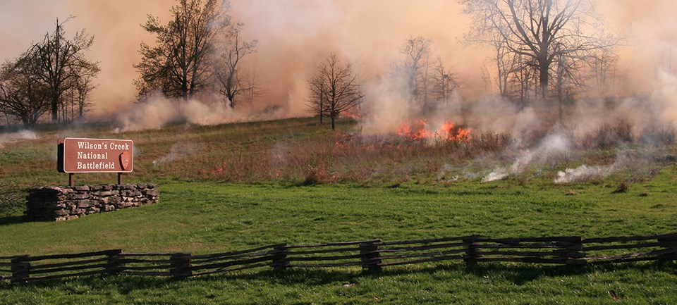 Flames in open field near Wilson's Creek National Battlefield sign.