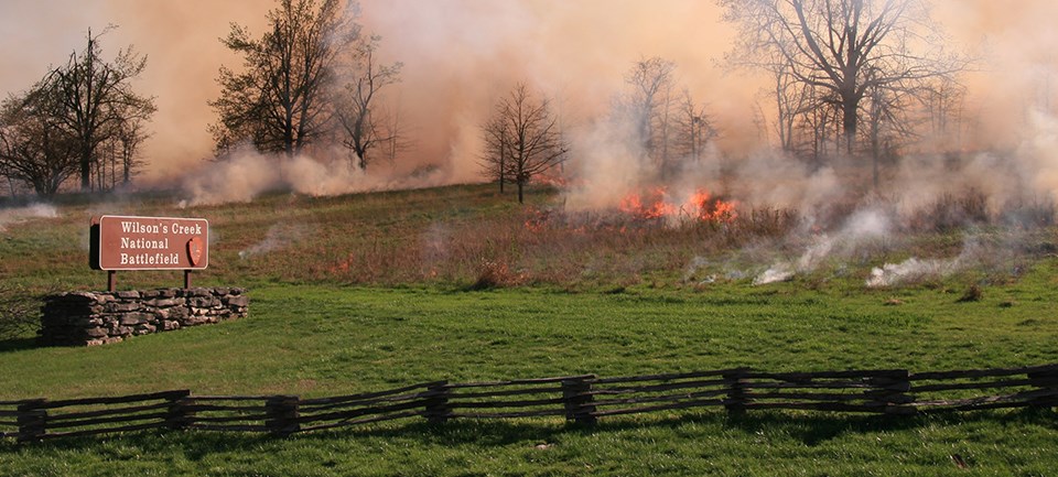 Wilson's Creek National Battlefield Prescribed Fire Flames in open field near Wilson's Creek National Battlefield sign.