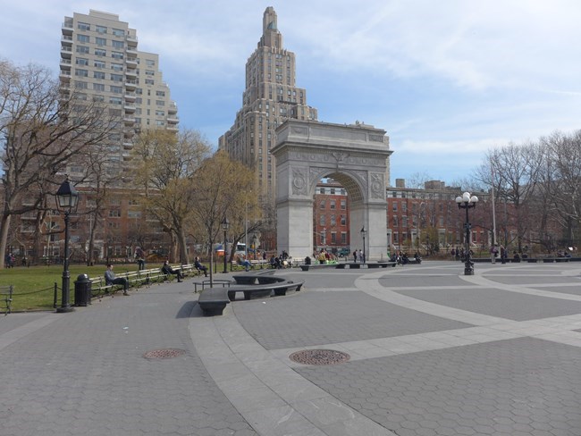 A paved surface with an arch in the distance and the Manhattan skyline