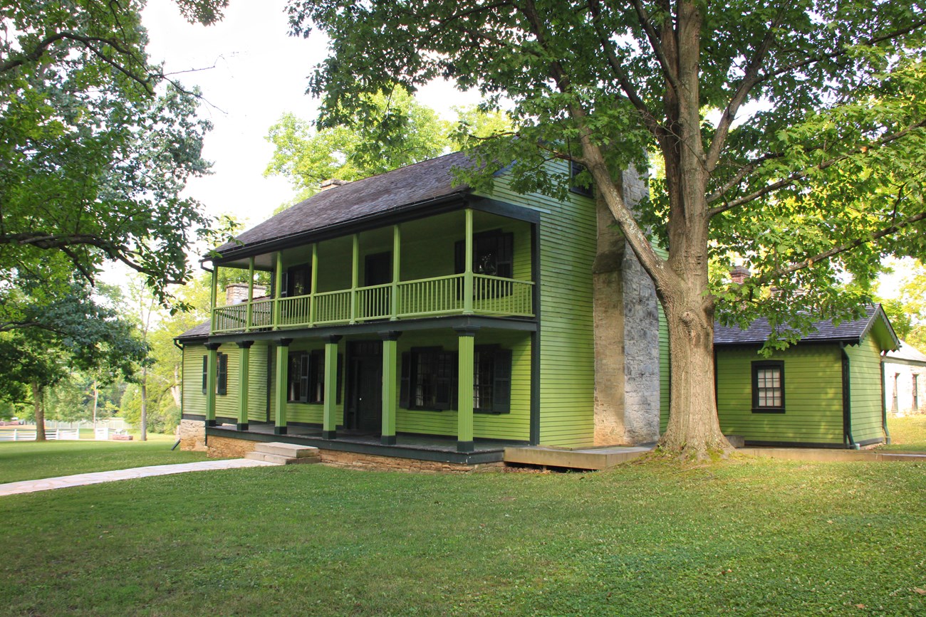 Photo of a two story bright green house flanked by mature hardwood trees