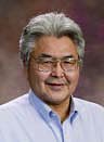 Alaskan Native man in blue shirt, short peppered hair and glasses.