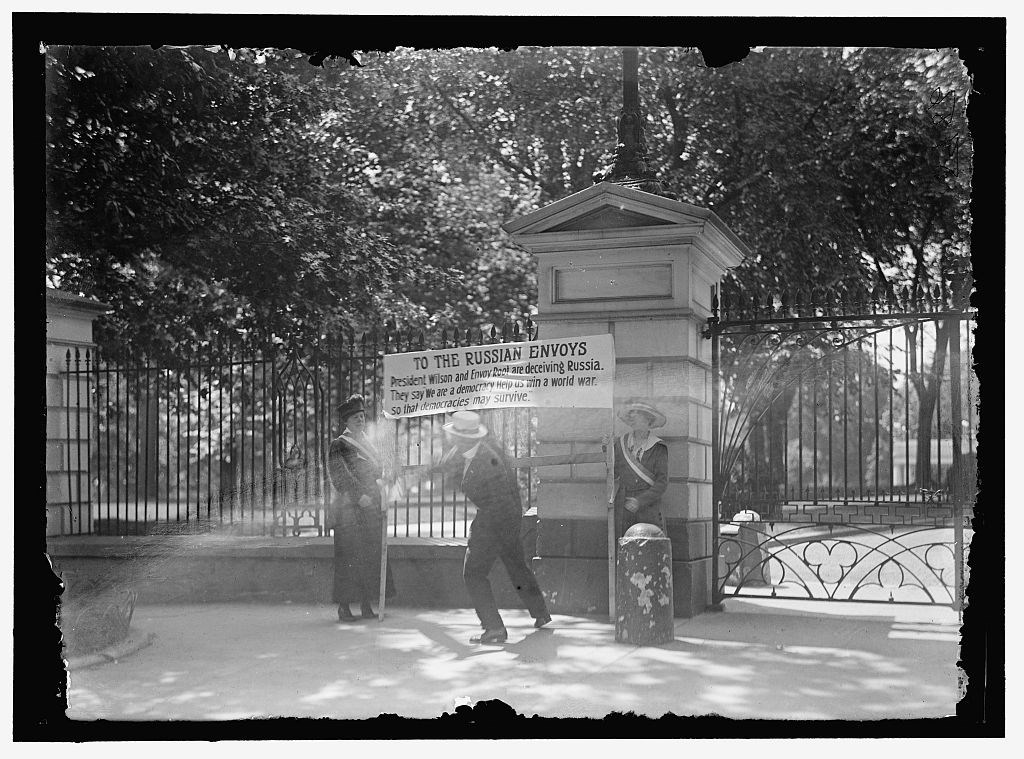 Man attacking a women's suffrage banner. The banner reads, "To the Russian Envoys President Wilson and Envoy Root are deceiving Russia. They say We are a democracy. Help us win a world war. so that democracies may survive."