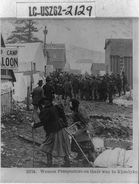 A group of people head to the Klondike, with two women pulling a sled of supplies