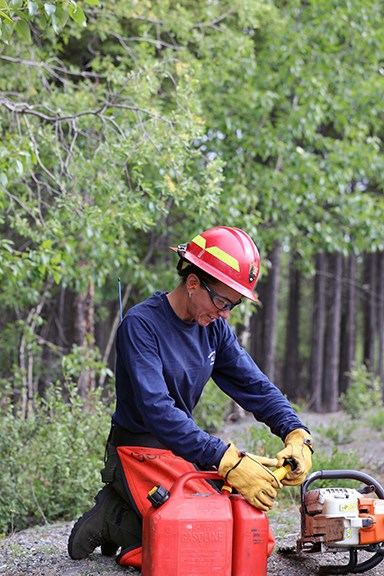 Kim Wong A female firefighter leans over her chainsaw to do a maintenance check and to fill it with gas and bar oil.