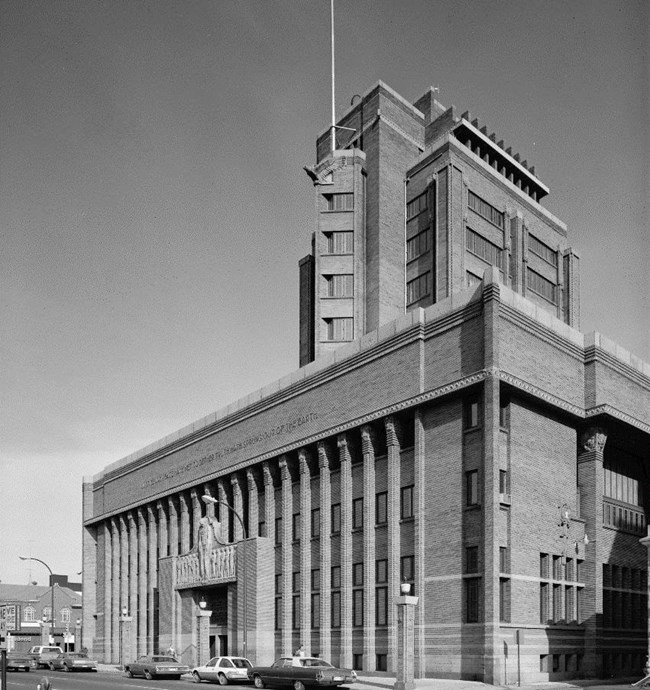 B&W photo of a brick and granite building, 8 stories high and fills a city block.