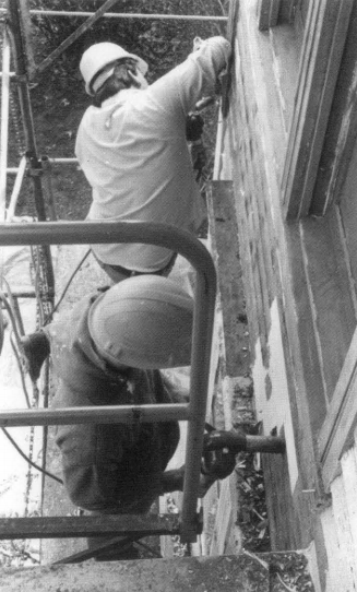Workers on scaffolding removing paint Two men on scaffolding removing paint from a wall.