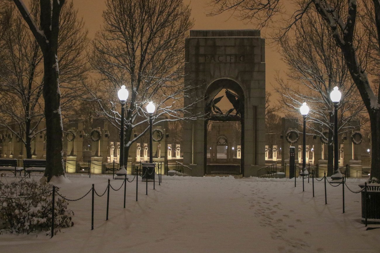 A night time photo of the street lamps leading up to the World War II Memorial. The sky is clearly lit by out of sight light sources.