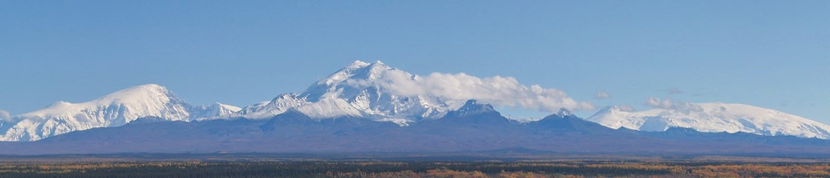 A large snow-capped peak dominates a landscape.
