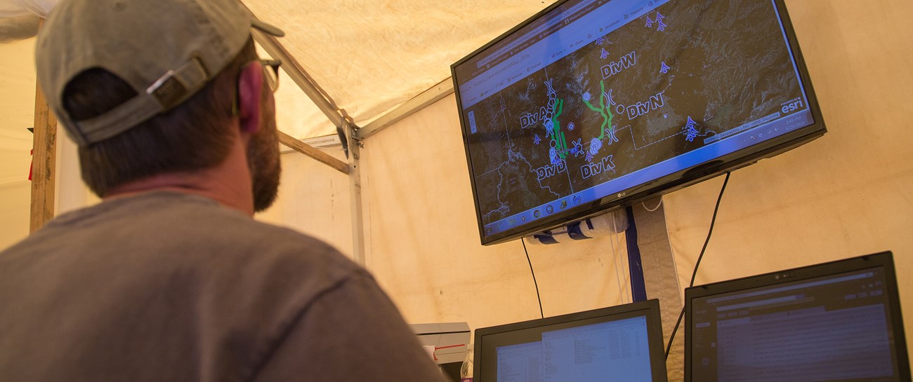 A man sits in front of three computer monitors looking at an online map.