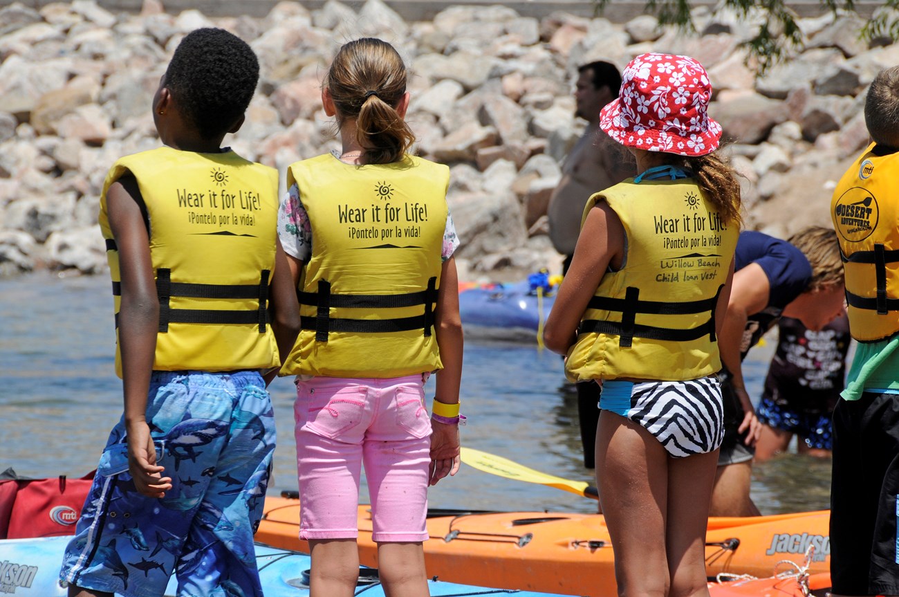 Kids standing near water and kayaks wearing life jackets
