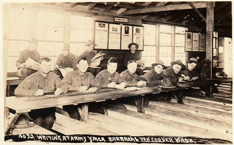 YMCA letters Black and white image of soldiers sitting at a long table writing letters.