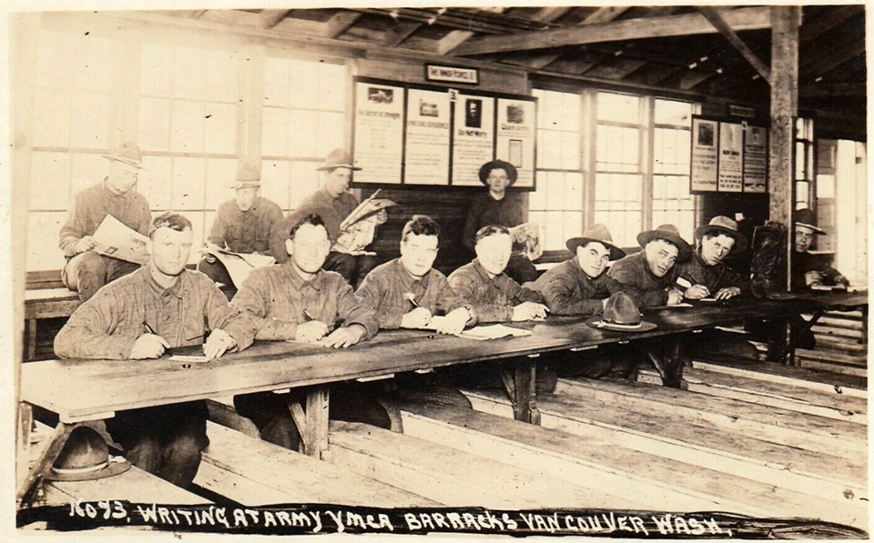 YMCA letters Black and white image of soldiers sitting at a long table writing letters.