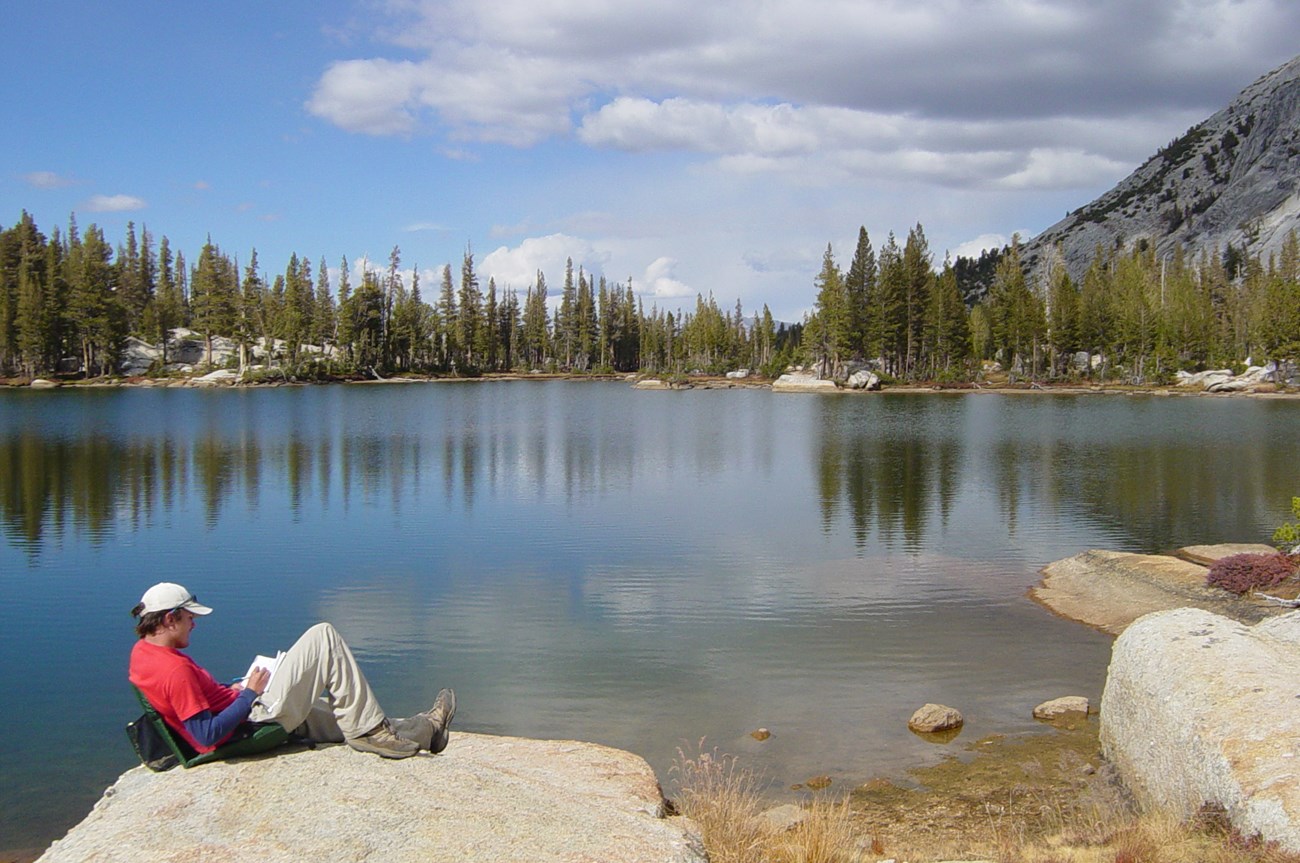 Man enjoys mountain lake Man sits next to mountain lake