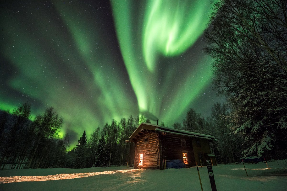 Northern lights over a cabin in the snowy woods