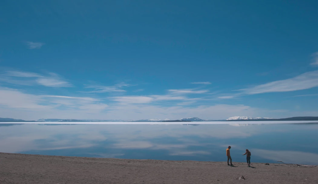 Yellowstone Lake Two people on the beach of a very large lake with snow-capped mountains in the background.